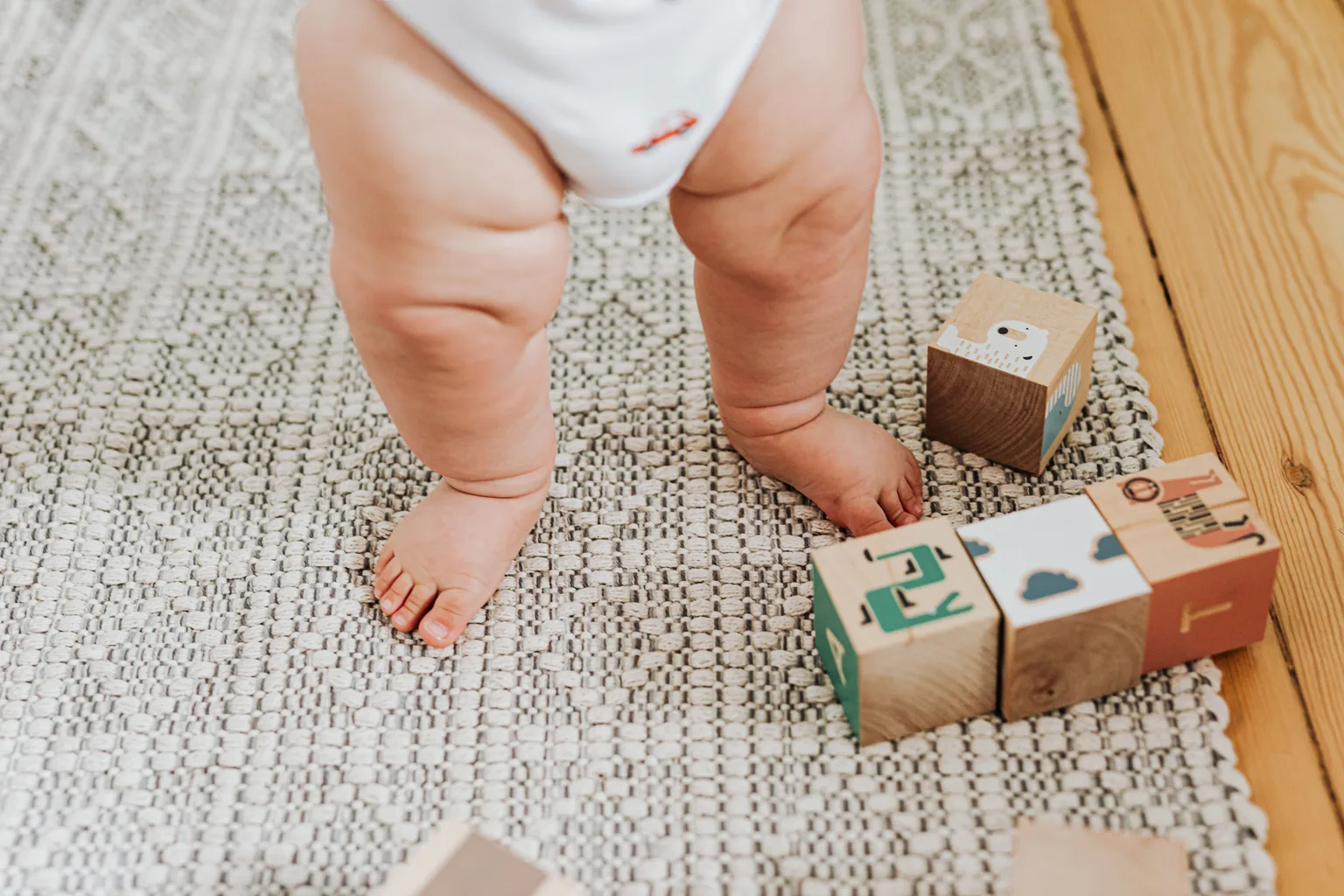 A baby's legs beside wooden building blocks on a soft indoor rug