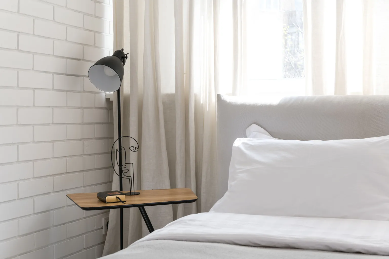 A calm minimalist bedroom with a made bed and a bedside lamp in soft daylight