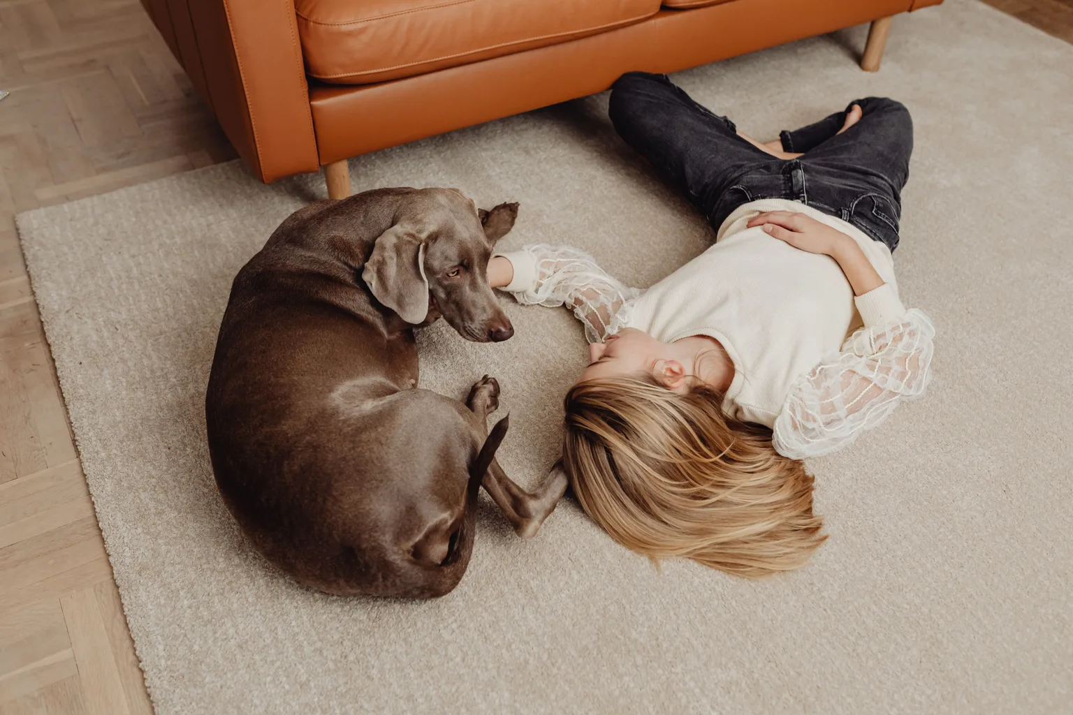 A child and a brown dog lying together on a light-colored living room carpet