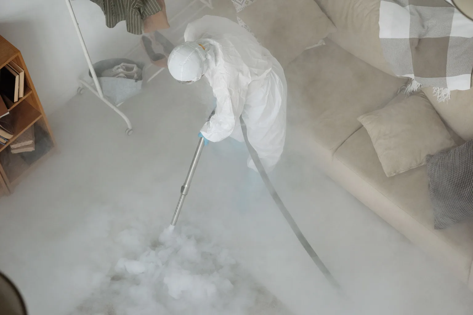A technician in protective clothing treating a rug in a living room