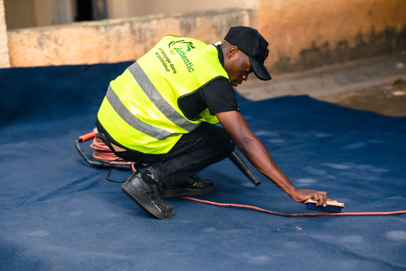A cleaning technician in a high-visibility vest working a brush across a large carpet