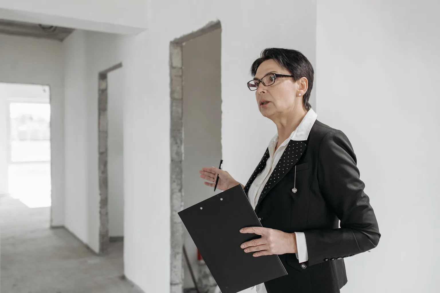 A person in business clothing holding a clipboard while inspecting an empty unfinished room