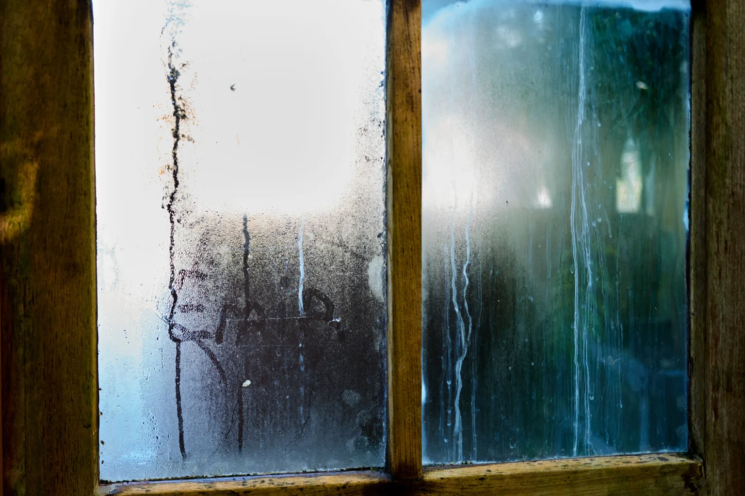 Condensation streaking down the inside of a wooden-framed window pane