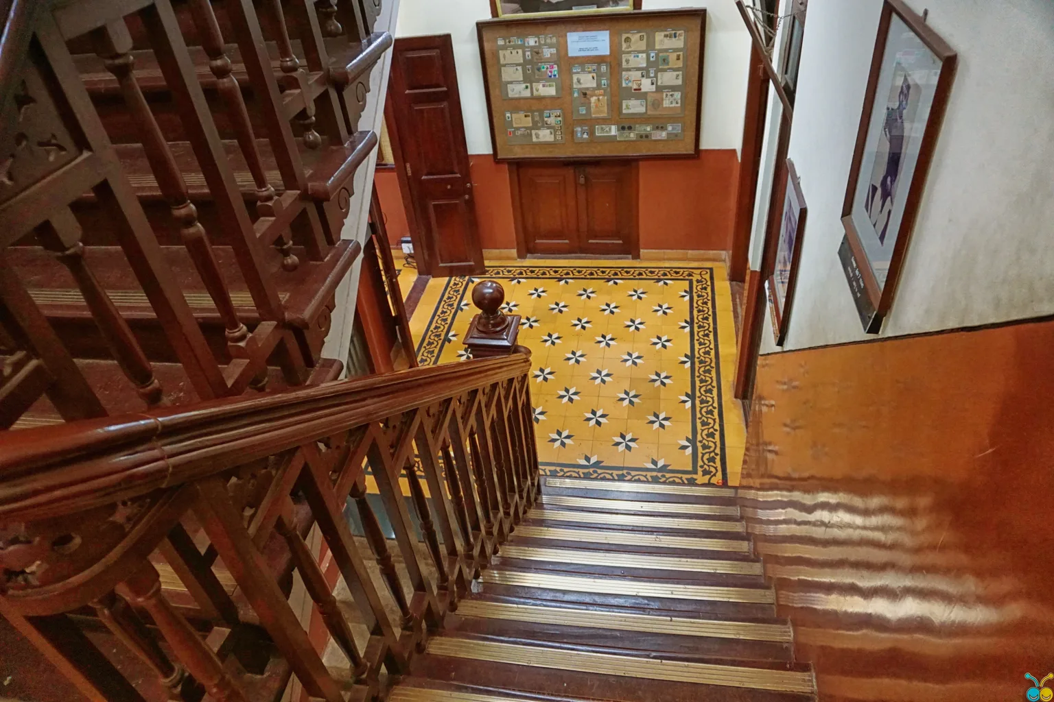 Ornate wooden staircase in a historic home looking down onto a patterned tile entry floor