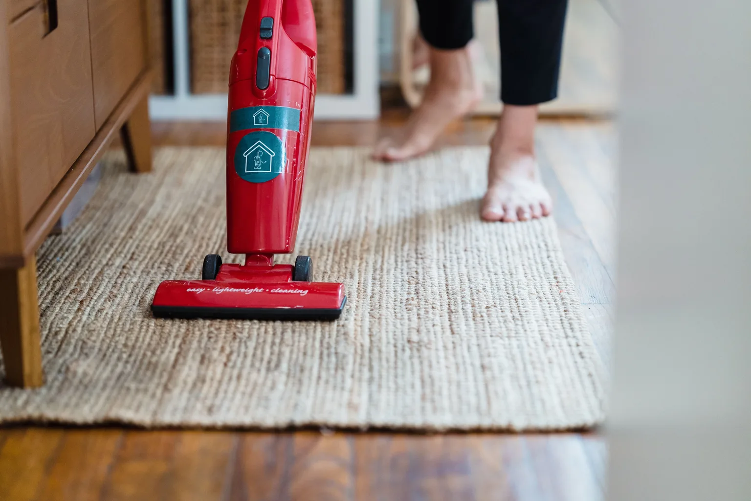 A red upright vacuum being pushed across a light-colored carpet in a home