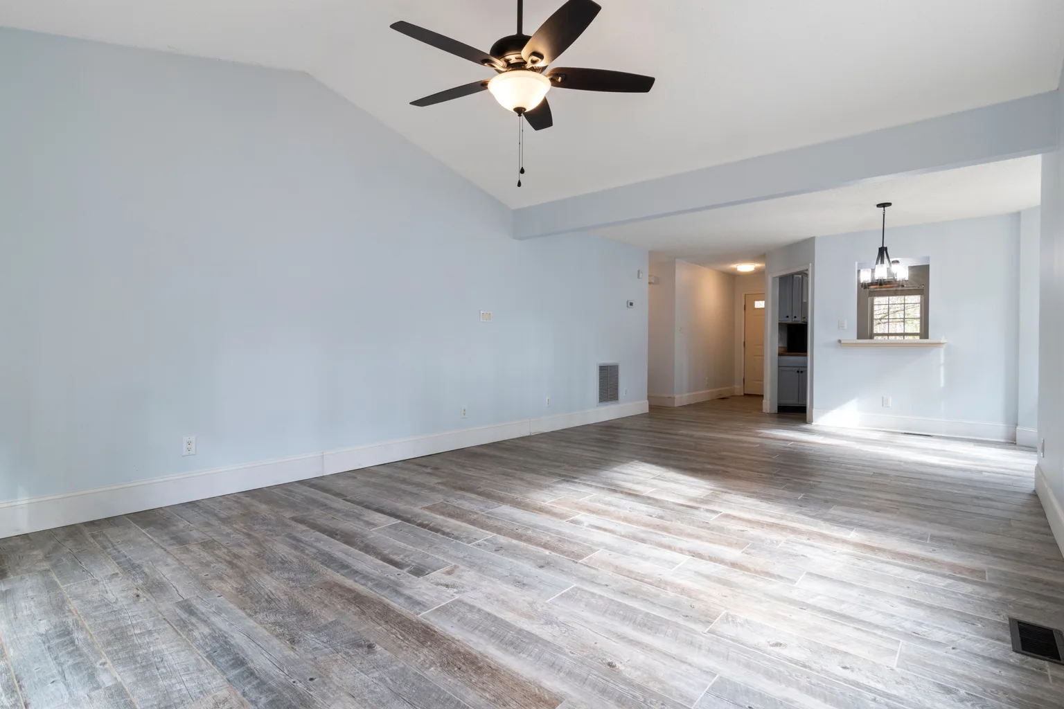 Bright empty living room with a wood floor and a ceiling fan running overhead
